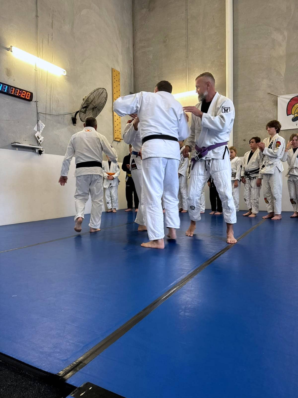 Adult members in gis working through a technique while a coach adjusts a grip