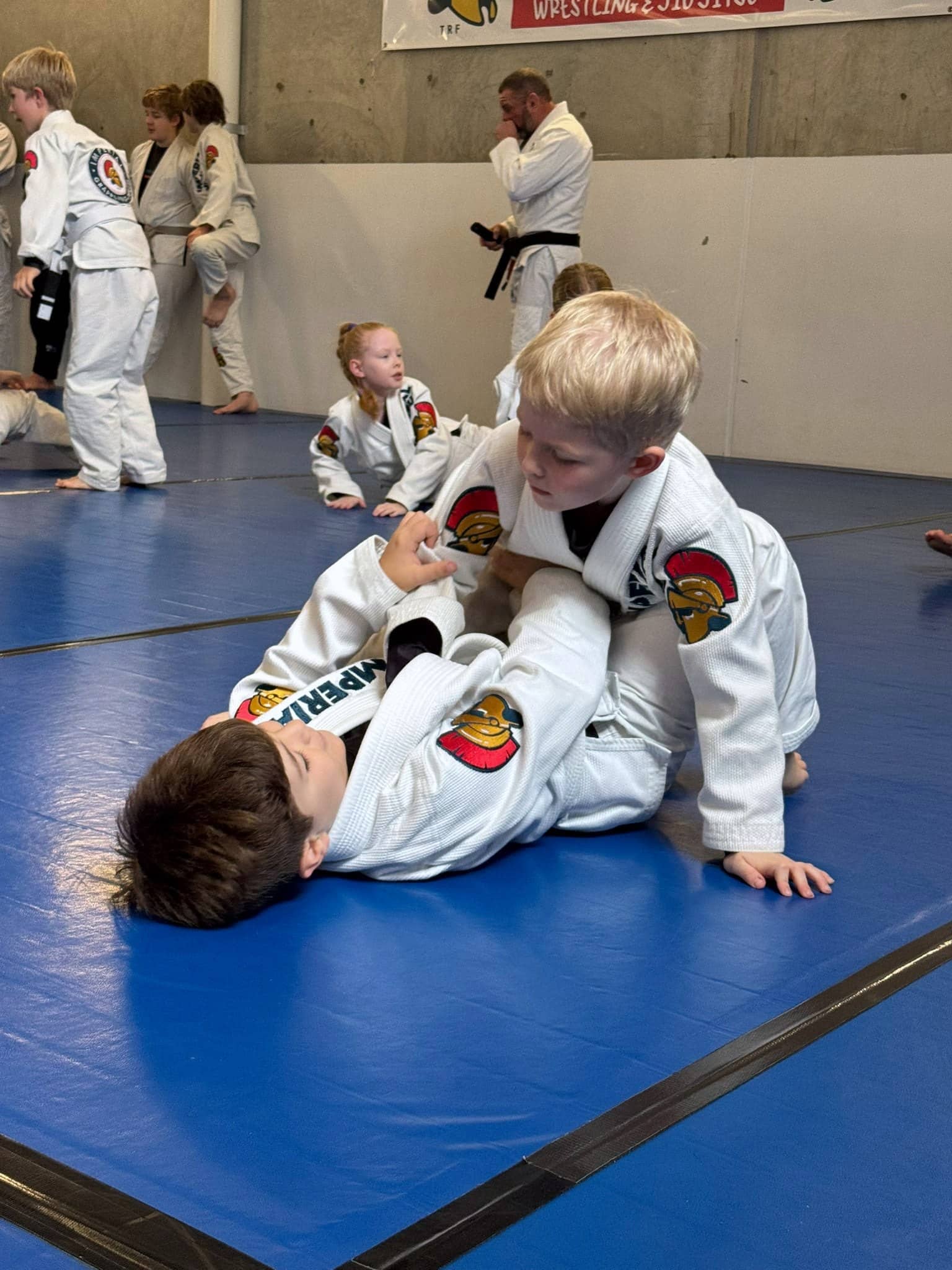Two small children mid-roll on the mats at Imperial Grappling Perth, one working from the top