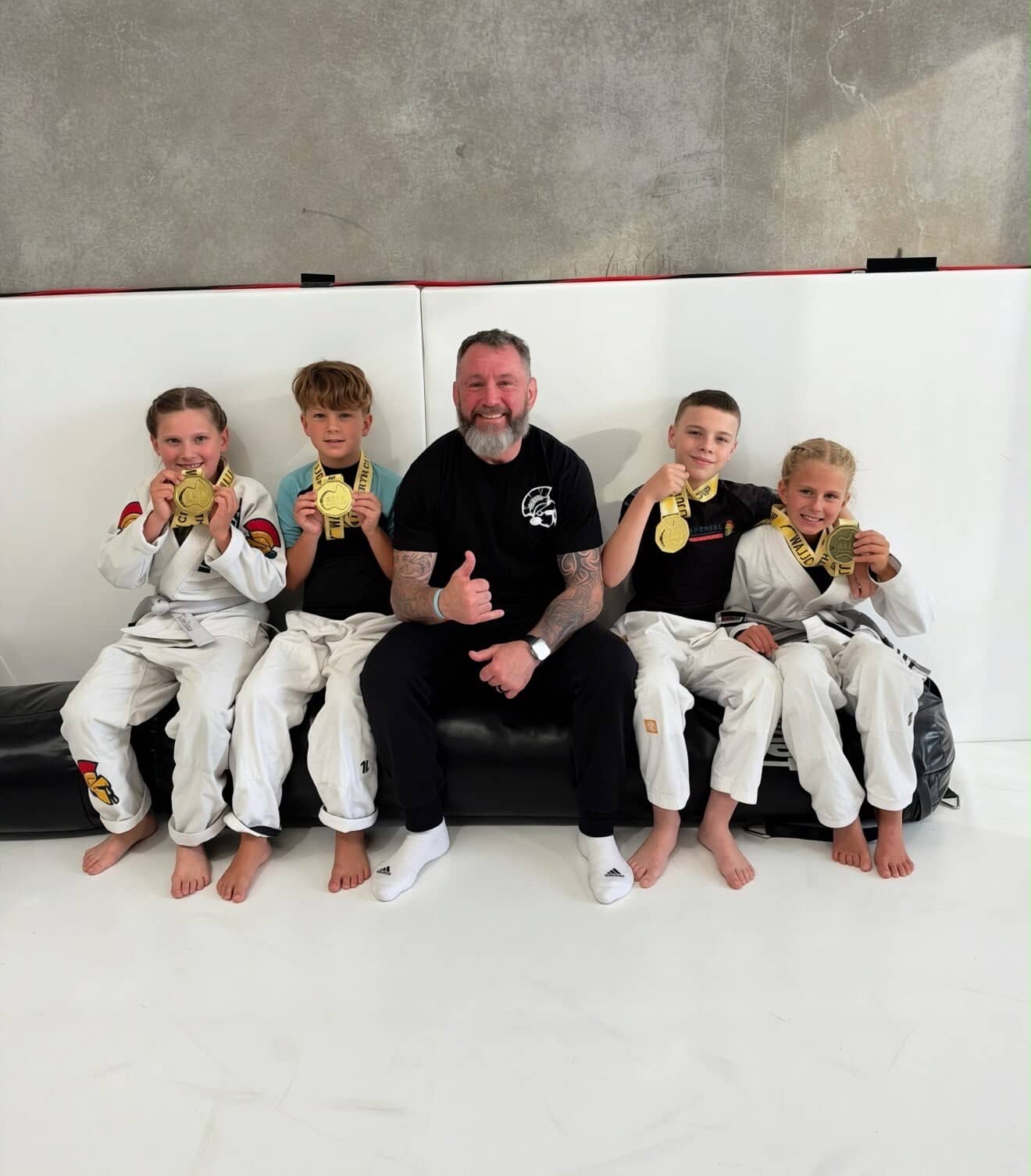 Head coach Adam Toole sitting with four young members at a competition, each of them holding up a medal