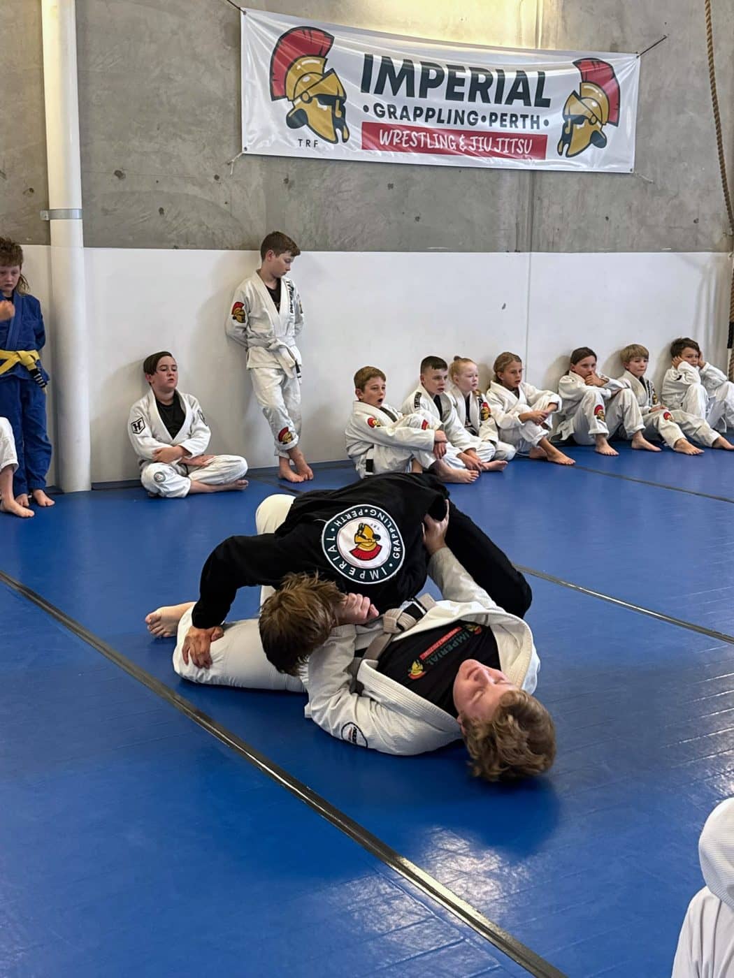 A junior working a pin on their partner mid-mat while the rest of the class watches
